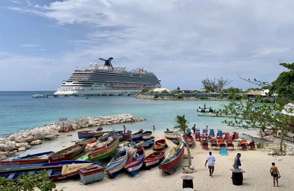 Image of fishing boats on a beach in Ocho Rios. In the background, a cruise shipped is at the pier.